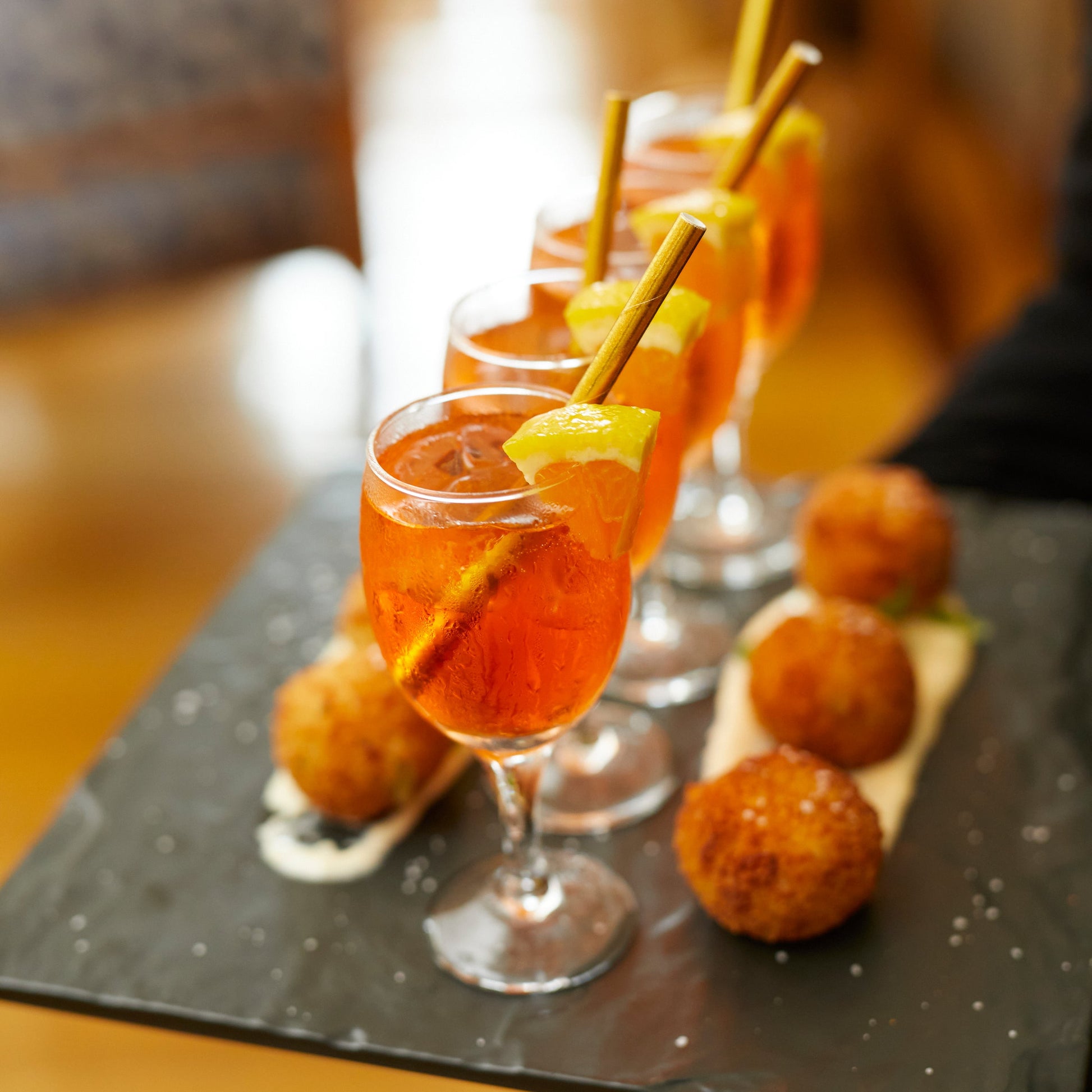Glasses of orange cocktails with lemon slices on a black slate board.